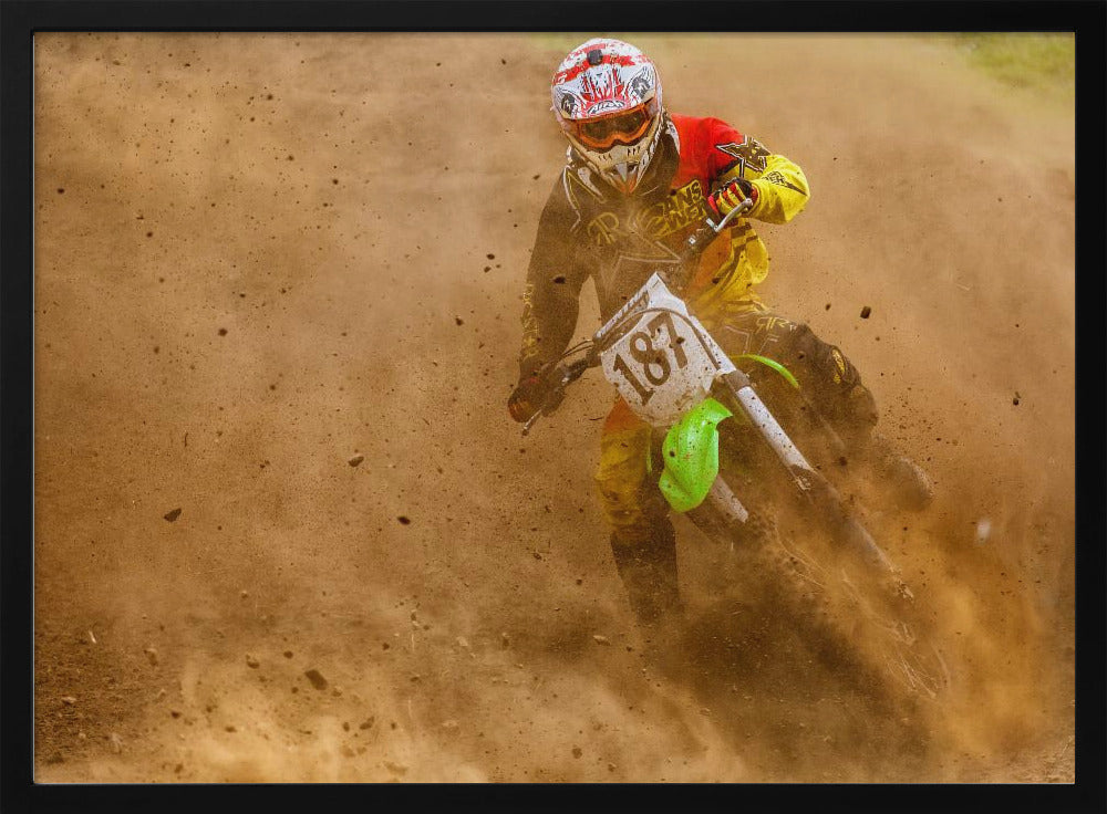 An action shot of a motocross rider in full red and yellow gear, speeding through a dirt track and kicking up a large cloud of brown dust and debris. Print