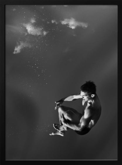 A dramatic black and white photograph of a male diver suspended mid-air in a tuck position. The background is a dark, atmospheric gray, with what appears to be clouds and bubbles, giving the impression of being underwater or in a vast, empty space. The lighting highlights the athlete's muscular physique. Artwork