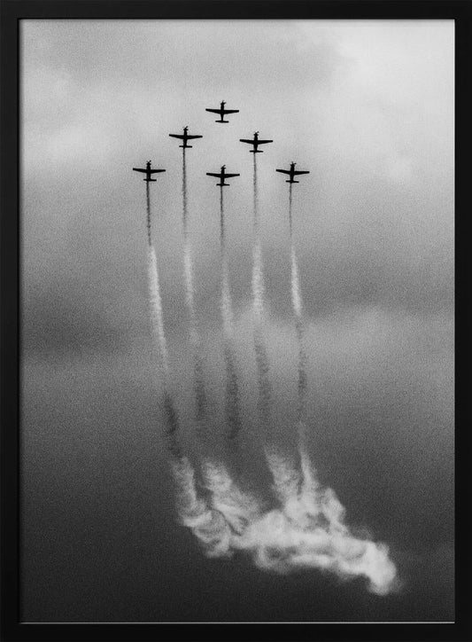 A grainy black and white photo of six airplanes flying in a V-formation against a cloudy sky. Each plane leaves a long, white smoke trail that billows at the bottom of the frame. The image is presented within a black border. Print