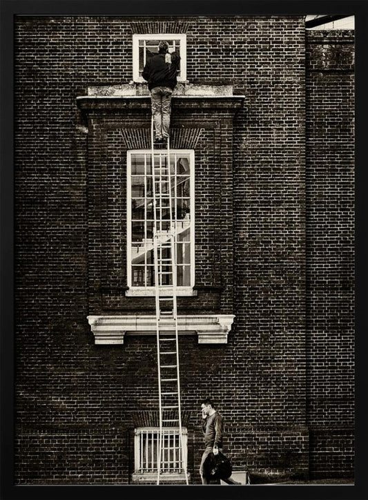 A striking black and white photograph of a man cleaning a small window high up on a brick building, standing precariously at the top of a very long ladder. Below, another man walks past on the street, seemingly unaware of the scene above. Artwork