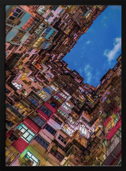 A dramatic worm's-eye view looking up at colorful, densely packed high-rise apartment buildings that create a geometric frame around a patch of deep blue sky. Wall Art
