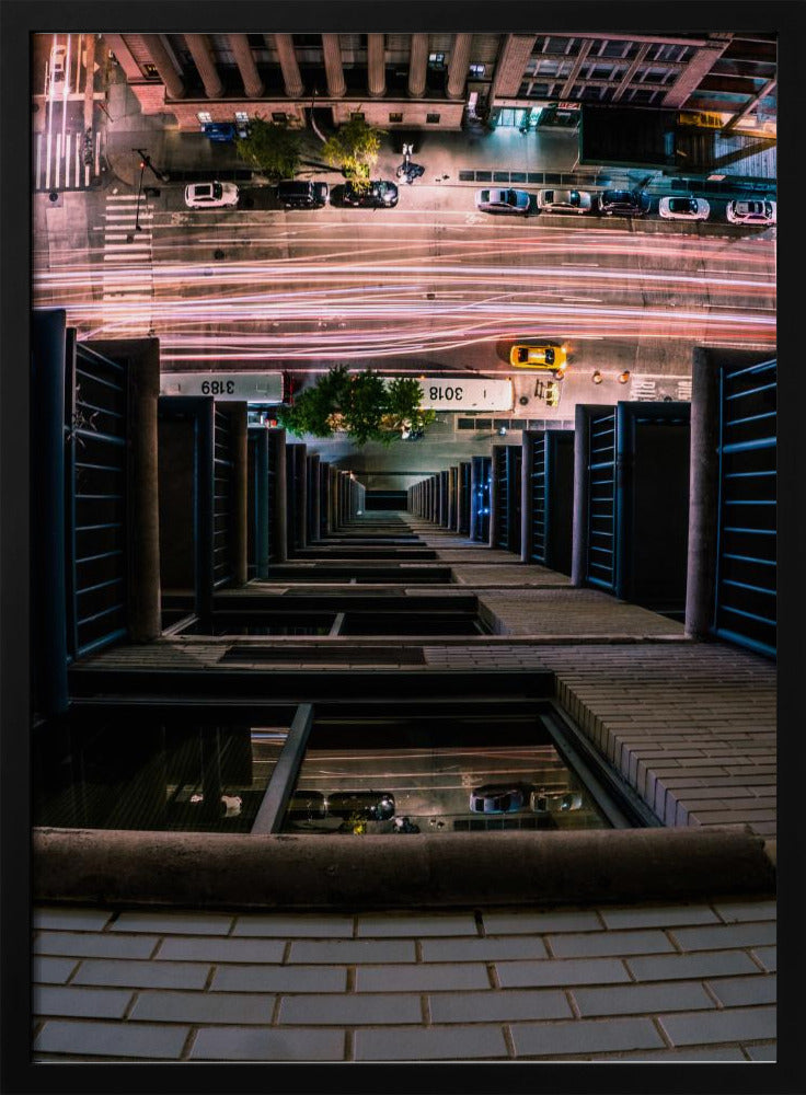 A dizzying bird's-eye view looking straight down the side of a skyscraper into a busy city street at night, with long exposure light trails from traffic creating streaks of red and white below. Wall Art