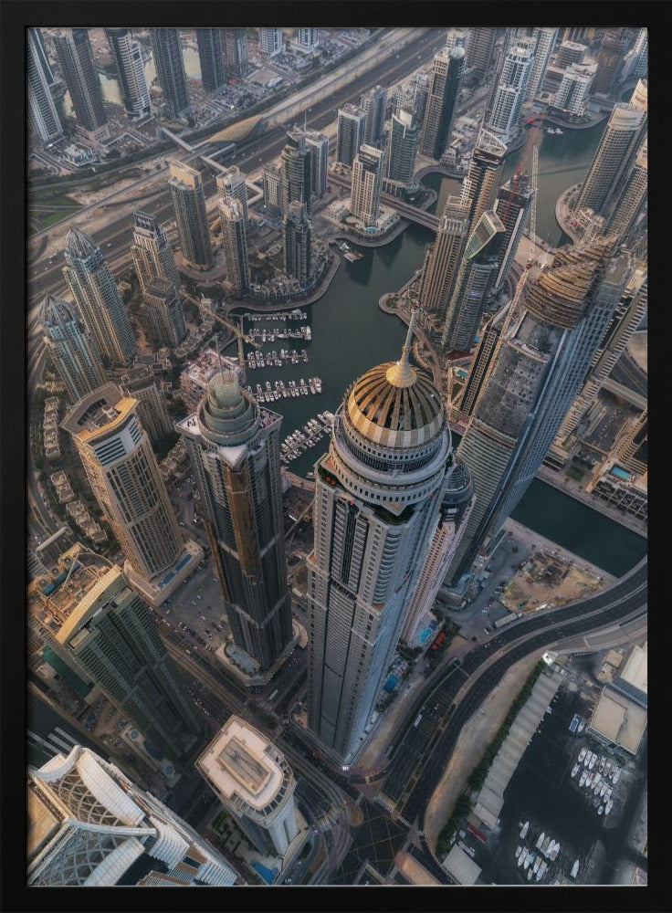 An aerial, bird's-eye view of the dense Dubai Marina, with towering skyscrapers casting long shadows. A waterway snakes through the urban canyon, with numerous yachts docked in the marina. A prominent skyscraper with a distinctive golden dome stands in the foreground. Artwork