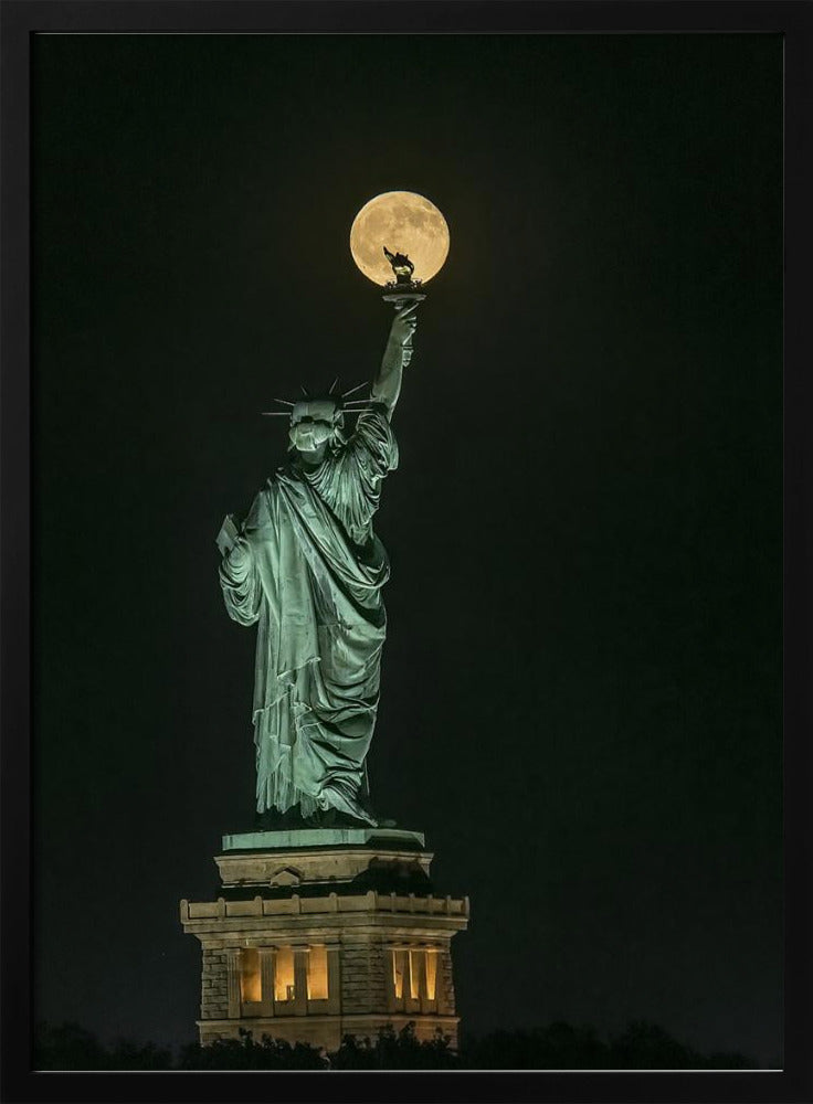 A striking night photograph of the Statue of Liberty, where a large, full yellow moon is perfectly aligned behind the torch, creating the illusion that the statue is holding up the moon. Artwork