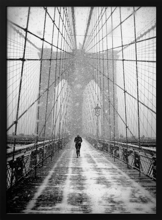 A vertical, black and white photograph of a solitary person walking along the Brooklyn Bridge during a heavy snowstorm. The iconic cables and towers of the bridge create a strong sense of perspective, drawing the eye towards the distant, hazy towers while snow falls all around. Artwork