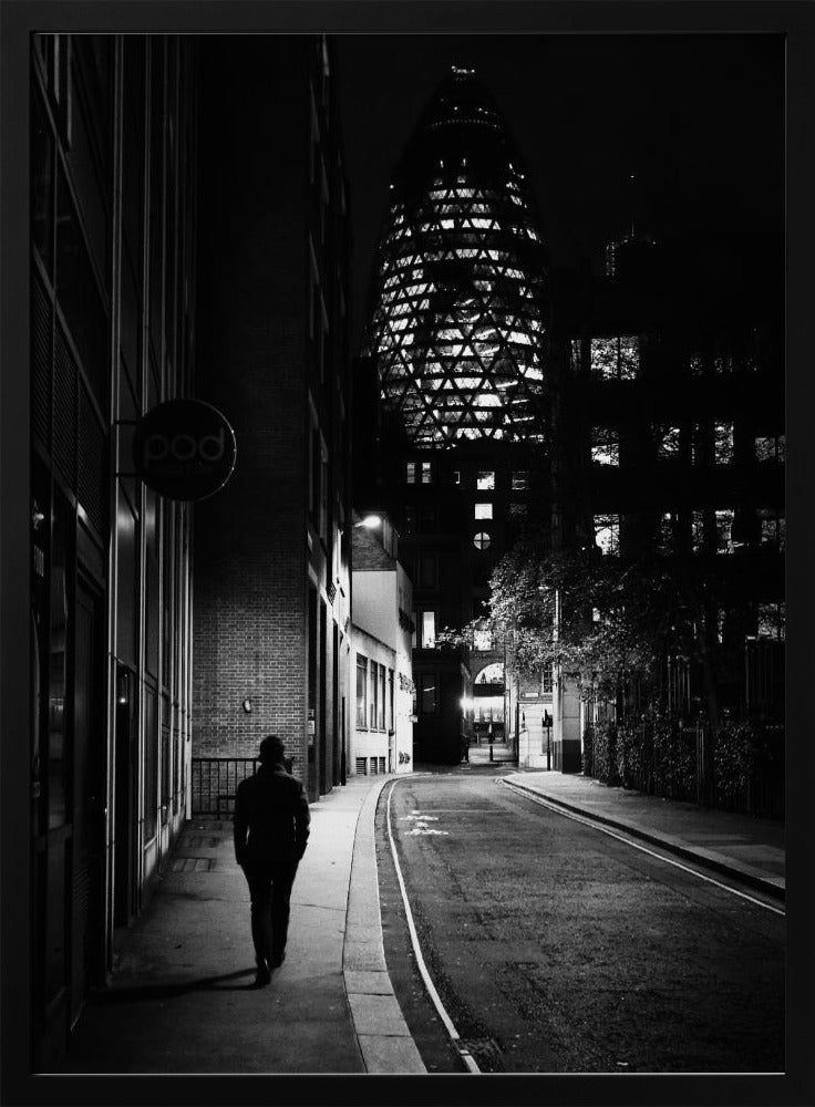 A moody black and white photograph of a person walking away down a narrow, deserted city street at night. In the background, the iconic Gherkin building in London is brightly lit against the dark sky. Wall Art