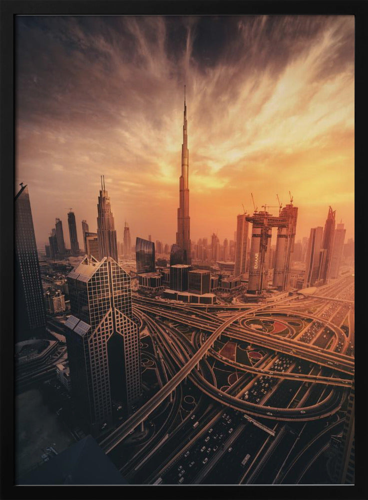 A dramatic high-angle photograph of the Dubai skyline at sunset. The Burj Khalifa stands tall in the center, bathed in the warm light of the setting sun, while a complex network of highways and interchanges weaves between modern skyscrapers in the foreground under a cloudy, orange-tinted sky. Poster