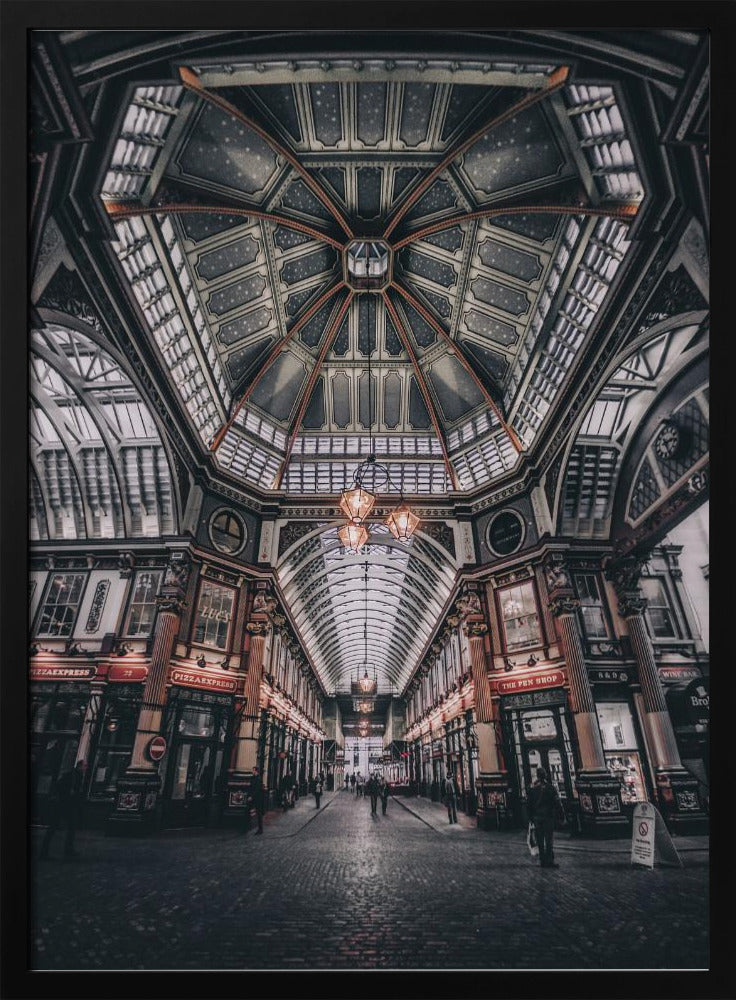 A wide-angle, symmetrical photograph looking down the center of an ornate Victorian covered market, Leadenhall Market. The focus is on the elaborate, arched glass and ironwork ceiling which is decorated in dark blue with gold stars. Below, a cobblestone path is lined with traditional shops with glowing lights, and a few people can be seen walking in the distance. The image has a moody, high-contrast aesthetic. Wall Art