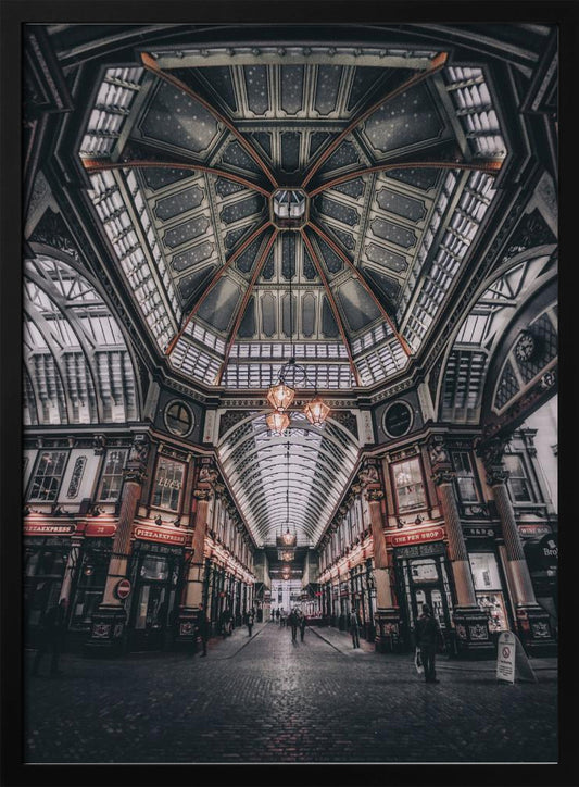 A wide-angle, symmetrical photograph looking down the center of an ornate Victorian covered market, Leadenhall Market. The focus is on the elaborate, arched glass and ironwork ceiling which is decorated in dark blue with gold stars. Below, a cobblestone path is lined with traditional shops with glowing lights, and a few people can be seen walking in the distance. The image has a moody, high-contrast aesthetic. Wall Art