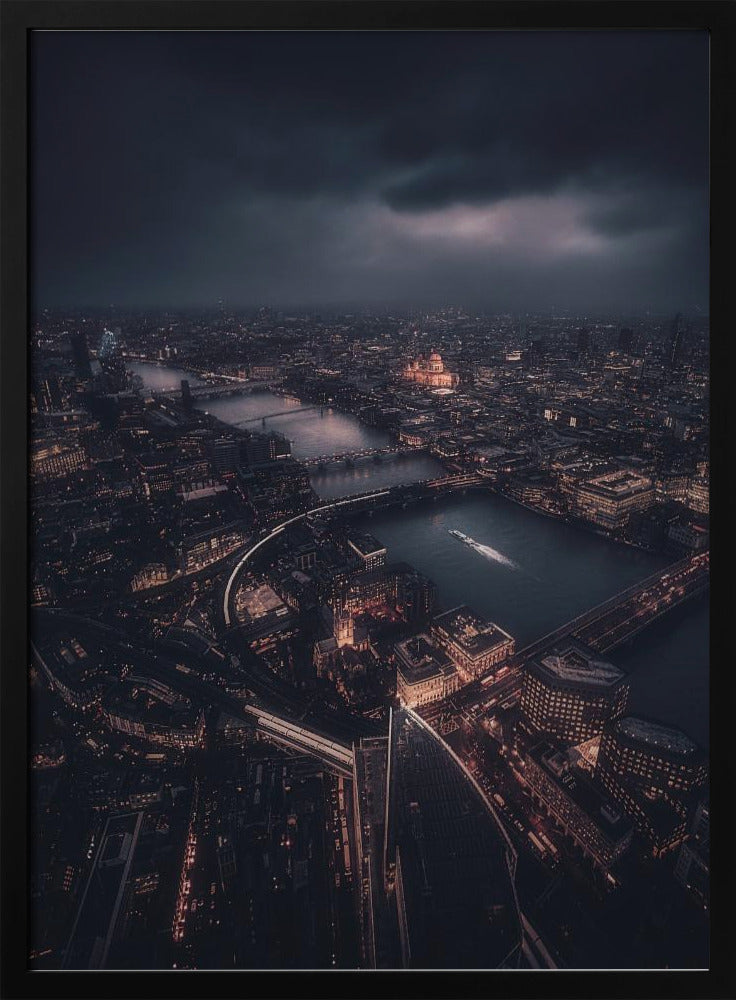 An aerial photograph of London at night from a high vantage point, overlooking the winding River Thames illuminated by the golden glow of city lights under a dark, dramatic, and cloudy sky. Wall Art