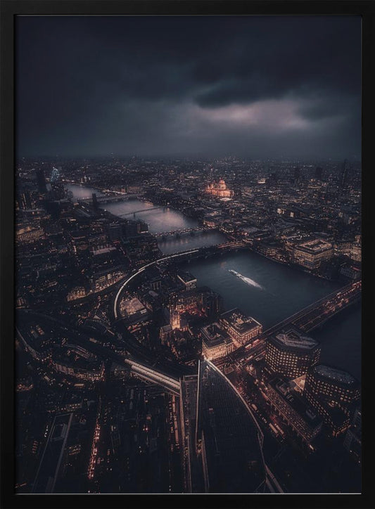 An aerial photograph of London at night from a high vantage point, overlooking the winding River Thames illuminated by the golden glow of city lights under a dark, dramatic, and cloudy sky. Wall Art