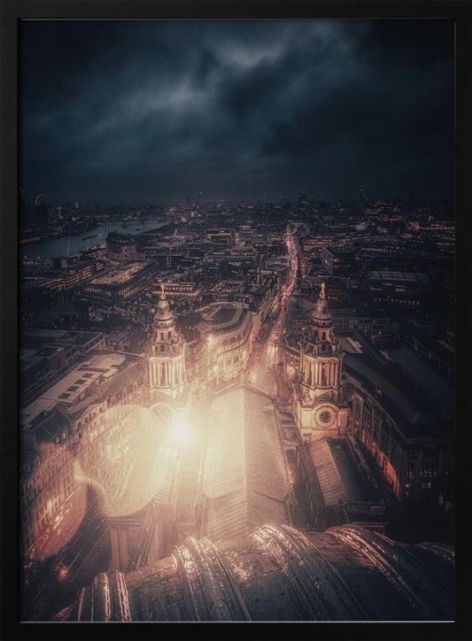 A dramatic, high-angle nighttime photograph of a sprawling city, likely London, viewed from the top of a cathedral. The foreground shows the curved dome, while below, two towers and the long roof of the church are brightly illuminated. The city stretches into the distance with countless golden lights under a dark, stormy, and cloud-filled sky. Poster
