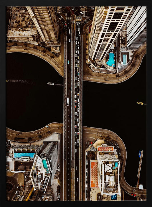 A symmetrical, top-down aerial photograph of a busy city bridge crossing dark water, flanked by towering skyscrapers with bright blue rooftop swimming pools. Print