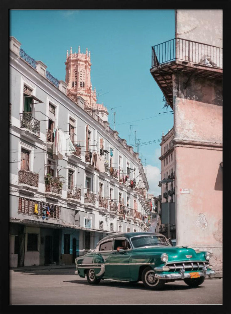 A vintage teal-green classic car sits on a sunny street in a historic city, possibly Havana, Cuba. Weathered apartment buildings with intricate balconies and hanging laundry line the street, with a peach-colored church tower visible in the background against a clear turquoise sky. Poster