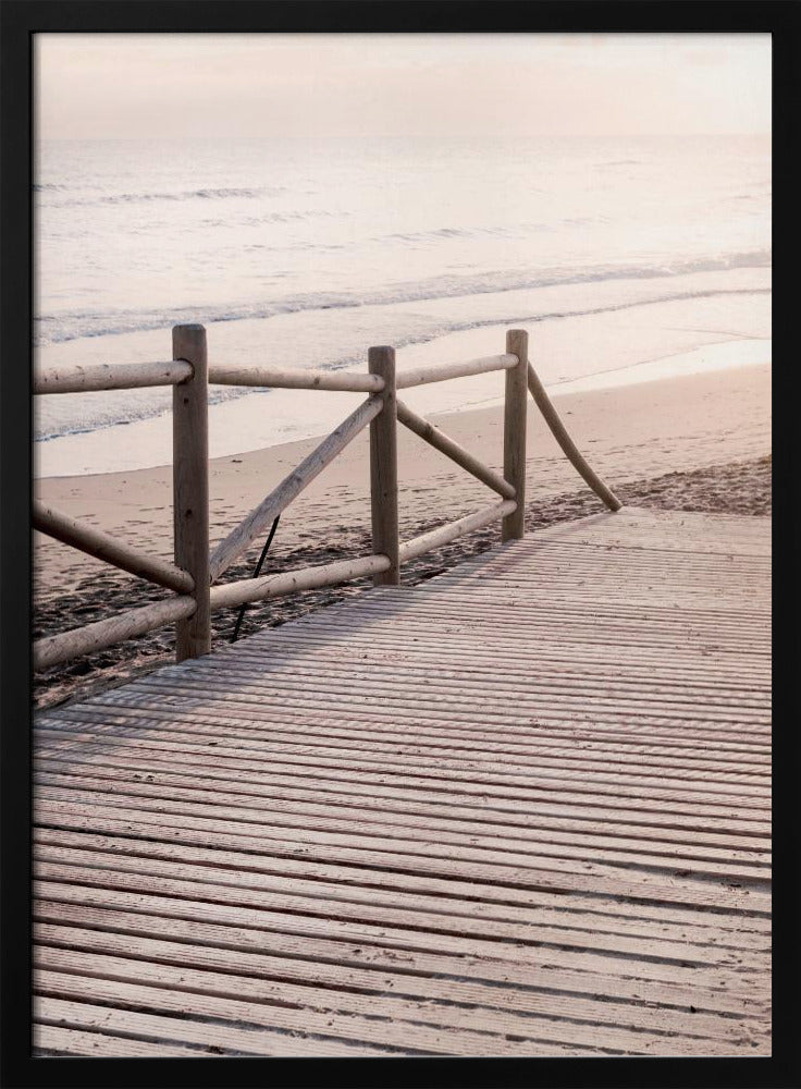 A wooden boardwalk with a rustic log fence leads down to a sandy beach with gentle waves lapping at the shore under a soft, hazy sunrise or sunset. Decor