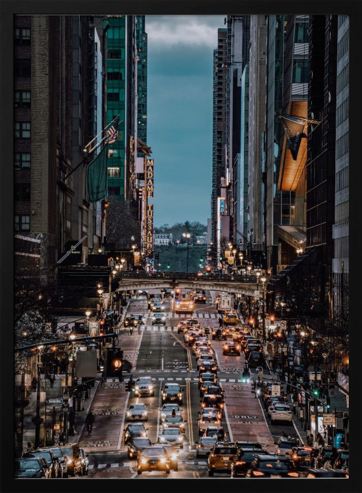 A high-angle, vertical photograph looking down a bustling New York City street at dusk, framed by towering skyscrapers. The street below is packed with cars, their headlights creating a warm golden glow, contrasting with the cool, dark blue tones of the twilight sky and buildings. Poster