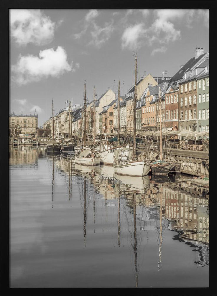 A muted, desaturated photograph of the Nyhavn harbor in Copenhagen. Old-fashioned sailboats are moored along the canal in front of a row of colorful historic buildings. The boats, buildings, and a cloudy sky are perfectly reflected in the calm water. Wall Art