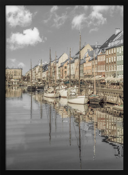 A muted, desaturated photograph of the Nyhavn harbor in Copenhagen. Old-fashioned sailboats are moored along the canal in front of a row of colorful historic buildings. The boats, buildings, and a cloudy sky are perfectly reflected in the calm water. Wall Art