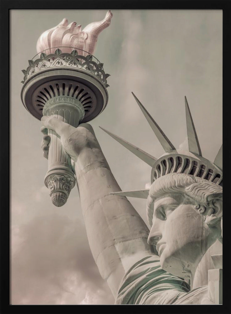 A low-angle, close-up photograph of the Statue of Liberty with a vintage color treatment. The shot captures her profile, crown, and her arm holding the torch aloft against a muted, cloudy sky, all enclosed in a thin black frame. Poster