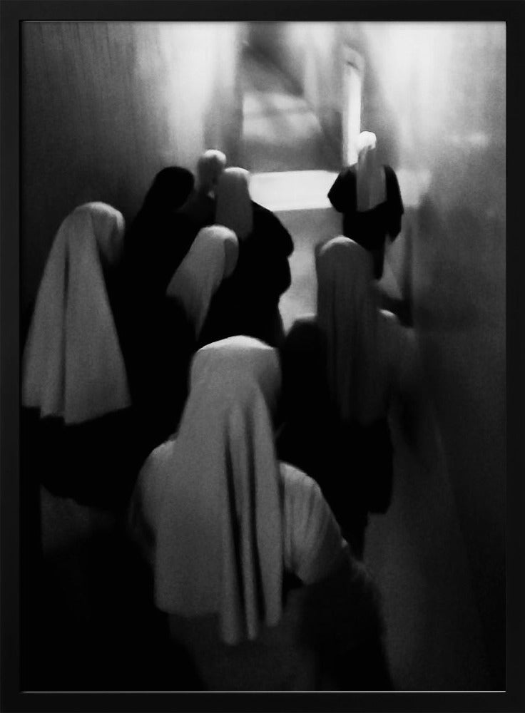 A mysterious black and white photograph captures a group of robed figures, possibly nuns, from above as they walk down a dark, narrow corridor. The image is blurred, creating a ghostly, ethereal atmosphere as the figures' white head coverings stand out against the deep shadows. Artwork