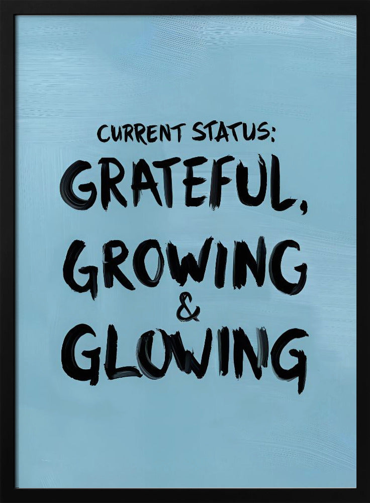 A motivational poster with a light blue background and a thin black frame. The text 'CURRENT STATUS: GRATEFUL, GROWING & GLOWING' is written in a bold, black, handwritten brush font. Decor