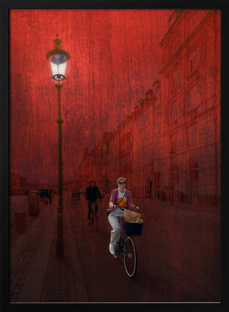 A surreal artistic image of a city street bathed in a textured red light. A woman rides a bicycle with a basket towards the viewer, while another cyclist is in the background. A tall, ornate lamppost is lit on the left side of the cobblestone street. Wall Art