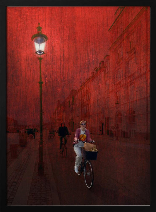 A surreal artistic image of a city street bathed in a textured red light. A woman rides a bicycle with a basket towards the viewer, while another cyclist is in the background. A tall, ornate lamppost is lit on the left side of the cobblestone street. Wall Art