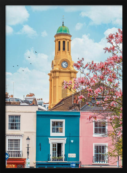 A vibrant city street scene on a sunny day, featuring a row of colorful houses in teal, pink, and off-white. A striking yellow clock tower with a green dome stands tall against a bright blue sky, with a blooming pink magnolia tree in the foreground. Print