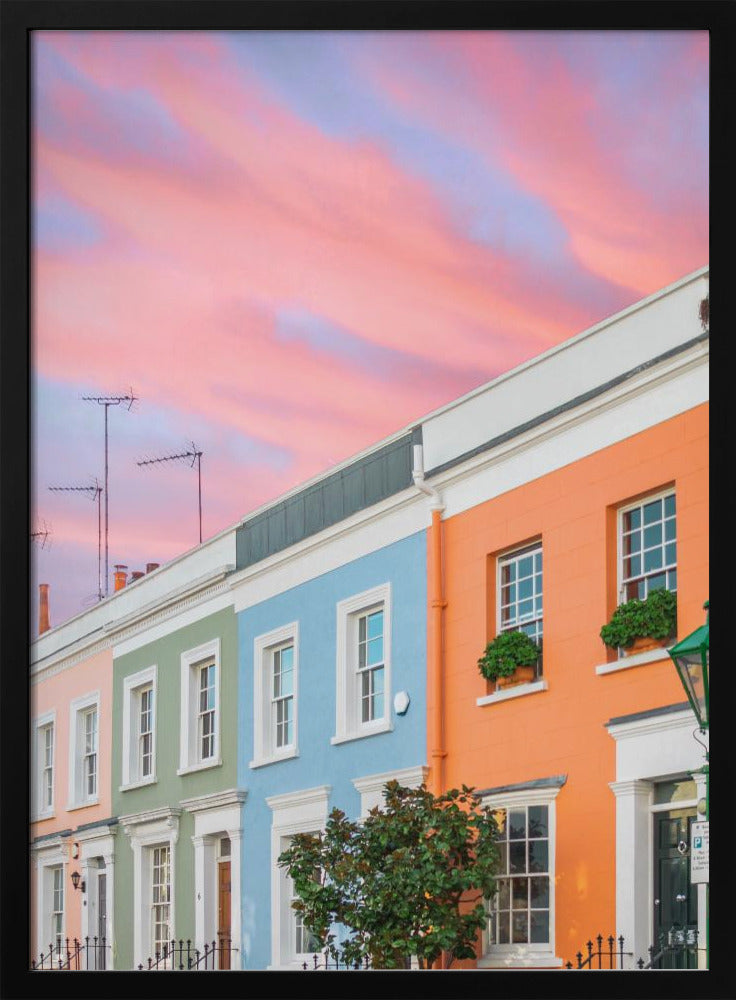 A row of colorful pastel townhouses in shades of orange, blue, green, and pink, viewed from a low angle against a dramatic, cloudy pink and purple sunset sky. Poster