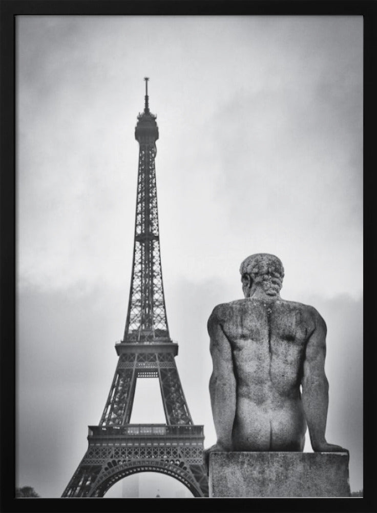 A black and white photograph capturing a contemplative scene in Paris, with the back of a seated, muscular male stone statue in the foreground looking towards the iconic Eiffel Tower which stands tall against a cloudy sky. Print