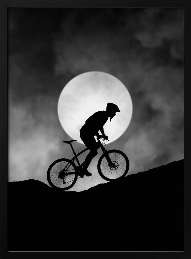 A dramatic black and white silhouette of a mountain biker riding uphill against the backdrop of a large, full moon in a cloudy night sky. Decor