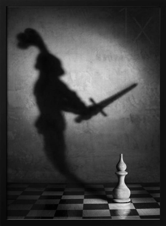 A black and white conceptual photograph of a single white chess piece on a checkerboard, casting a large, ominous shadow of a medieval knight holding a sword against a textured wall. Print