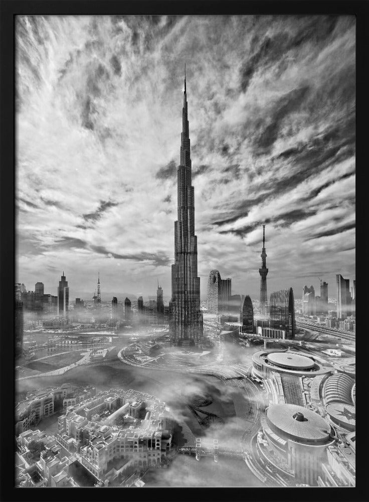 A dramatic black and white high-angle photograph of the Burj Khalifa dominating the Dubai cityscape, with swirling clouds above and a light mist surrounding the buildings below, all enclosed in a black frame. Poster