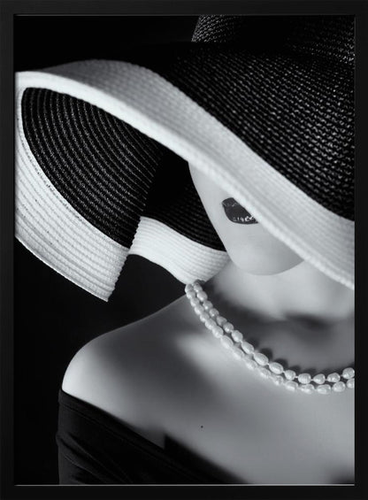 A glamorous black and white close-up photo of a woman wearing a large, striped sun hat that hides her eyes, revealing only her dark lips. She wears a pearl necklace and an off-the-shoulder top against a dark background, creating a mysterious and elegant mood. Wall Art