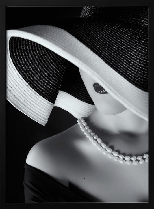 A glamorous black and white close-up photo of a woman wearing a large, striped sun hat that hides her eyes, revealing only her dark lips. She wears a pearl necklace and an off-the-shoulder top against a dark background, creating a mysterious and elegant mood. Wall Art