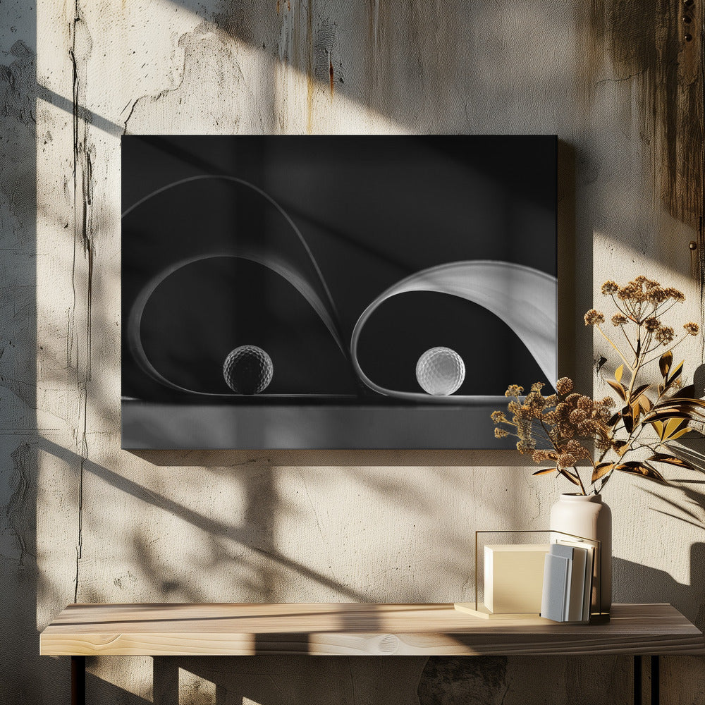 A framed, black and white abstract photograph featuring two golf balls nestled within the graceful curves of a single sheet of paper, creating a striking interplay of light, shadow, and form against a dark background. Decor