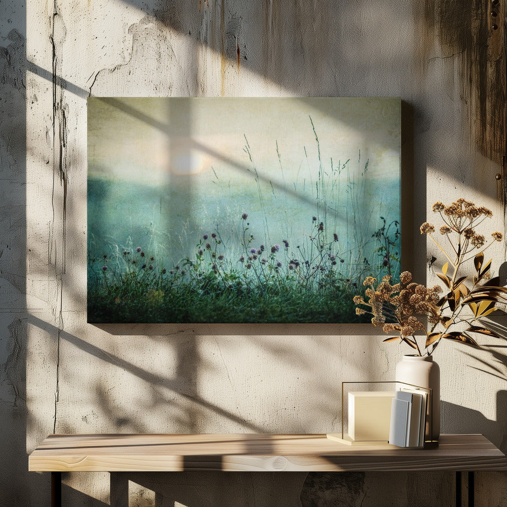 A framed photograph of a misty meadow at sunrise. The soft, pale sun hangs in a hazy, textured sky. In the foreground, tall green grasses and small purple wildflowers are in soft focus, creating a serene and dreamy atmosphere. Decor