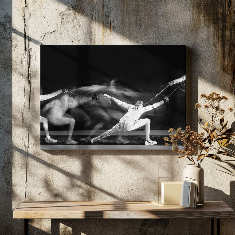 A framed, dramatic black and white photograph using long exposure to capture a fencer in motion. The fencer, in full white gear, lunges forward, their form crisp at the end of the movement while a ghostly blur trails behind, illustrating their rapid advance against a black background. Decor