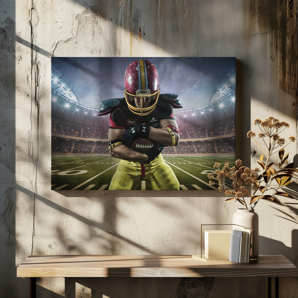 A framed poster of a determined football player in a red and yellow uniform standing on a field in a packed stadium. He is holding a football close to his chest with his head bowed, under bright stadium lights. Decor