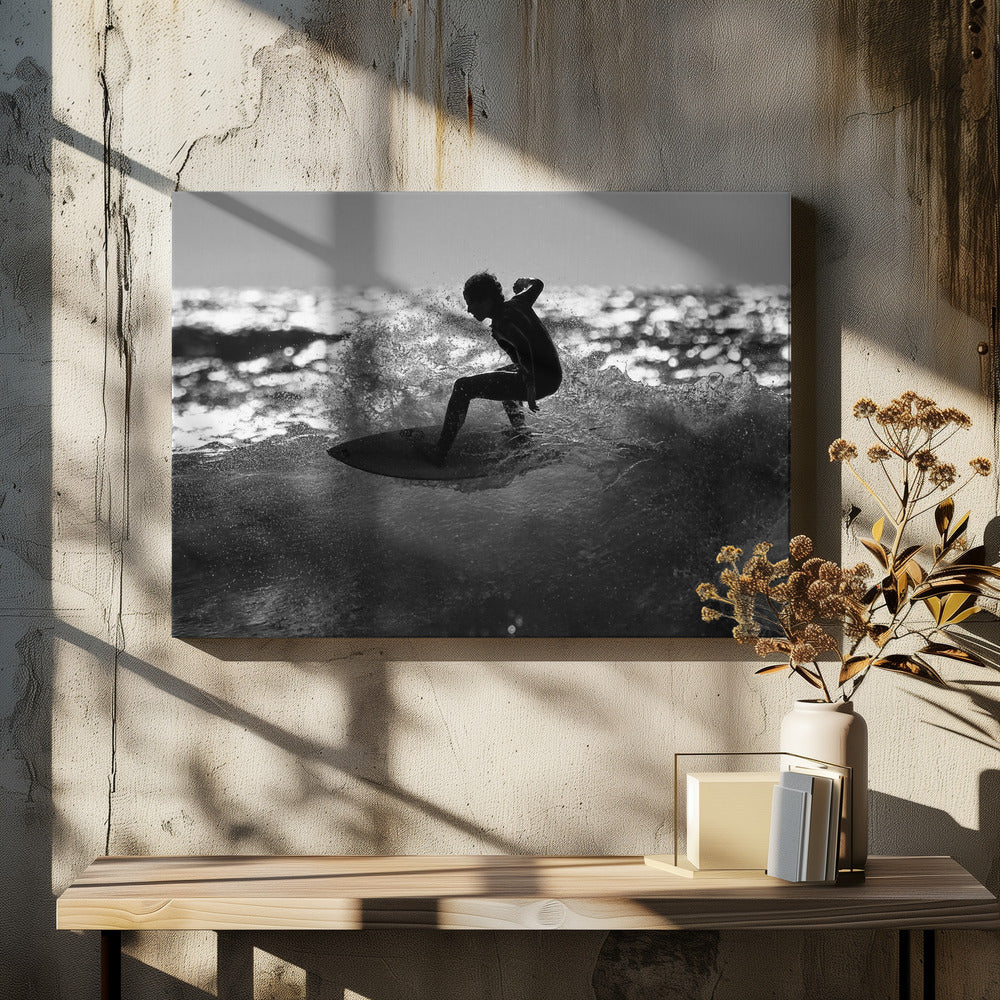 A black and white action shot of a surfer silhouetted against the sparkling ocean. The surfer is crouched low on their board, carving through a wave and creating a dramatic spray of water. The photo is enclosed in a silver frame. Print