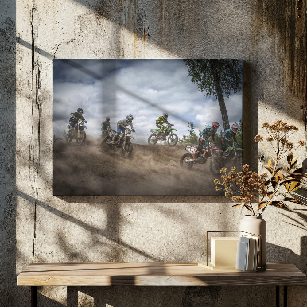 A dynamic action shot of several motocross riders racing up a dirt hill, kicking up a large cloud of dust. The riders are in full gear on colorful bikes, with a dramatic cloudy sky and a tall tree in the background. Print