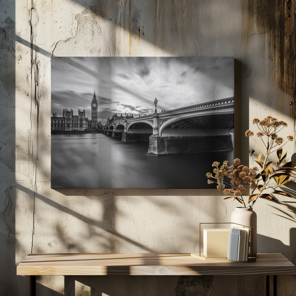 A dramatic black and white long-exposure photograph of London, featuring the smooth River Thames in the foreground, Westminster Bridge on the right, and the iconic Big Ben and Houses of Parliament on the left under a cloudy, streaked sky. The image is presented in a silver frame. Print