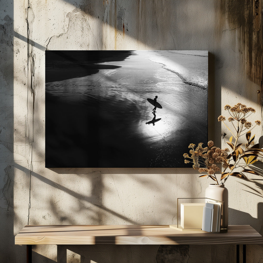 A high-contrast, black and white photograph of a silhouetted surfer carrying a surfboard and walking along the wet, reflective sand at the water's edge. Decor