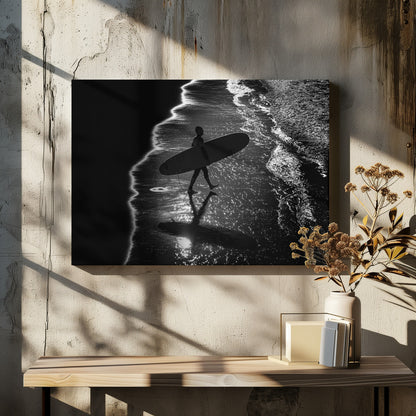 A dramatic, high-contrast, black and white aerial view of a silhouetted surfer carrying their surfboard along the shoreline. The sun glints off the wet sand and the dark water, creating a sparkling effect and a clear reflection of the surfer. Poster