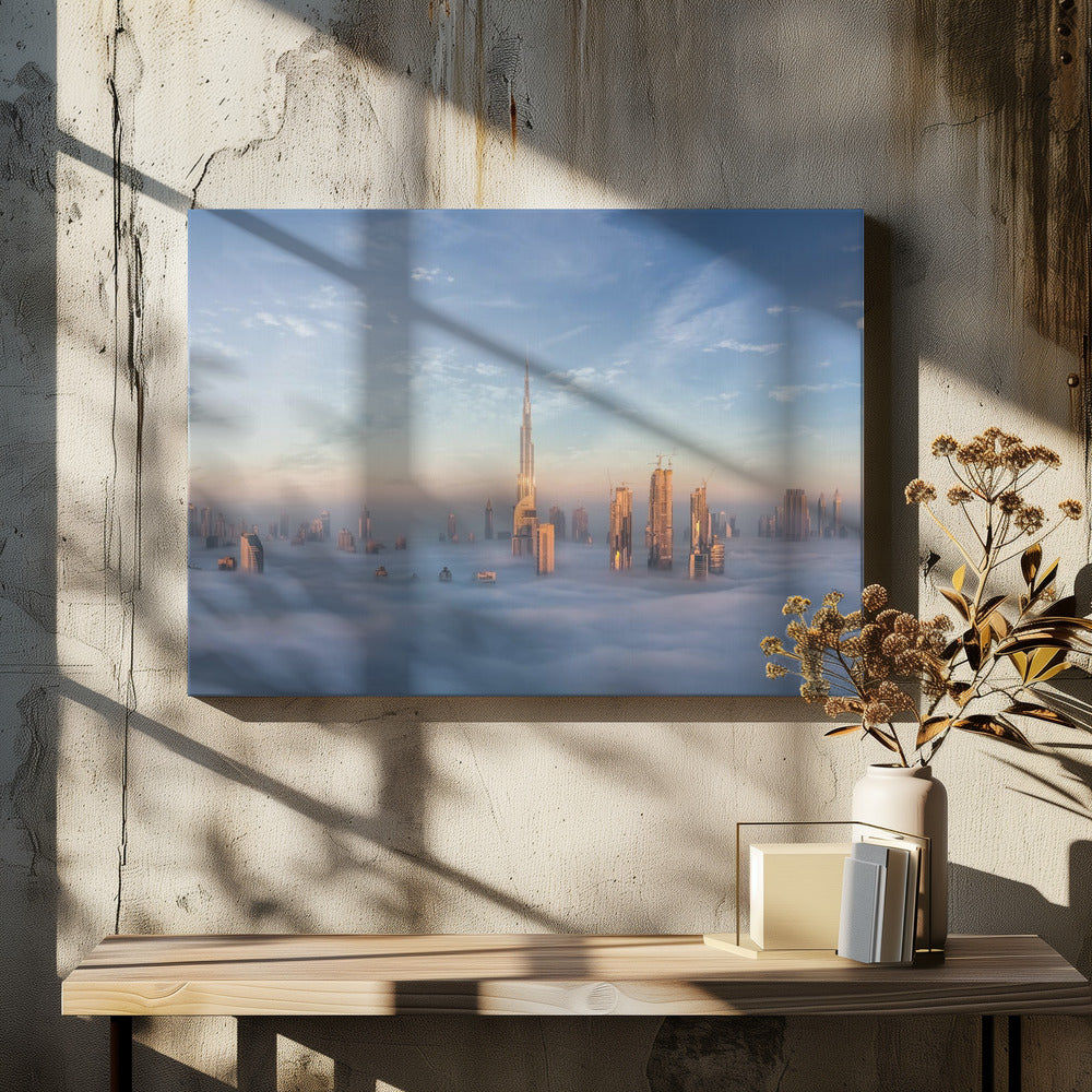 A framed photograph of the Dubai skyline, with the Burj Khalifa and other skyscrapers piercing through a thick blanket of low-lying clouds or fog. The scene is bathed in the warm, golden light of sunrise or sunset against a pale blue sky. Poster