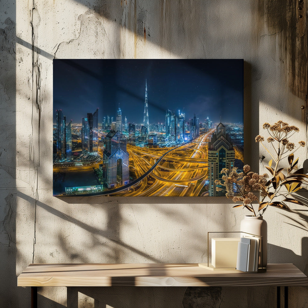A vibrant aerial photograph of the Dubai skyline at night, with the iconic Burj Khalifa towering in the center. A complex web of brightly lit highways with light trails from traffic dominates the foreground, weaving between modern skyscrapers under a starry night sky. Decor