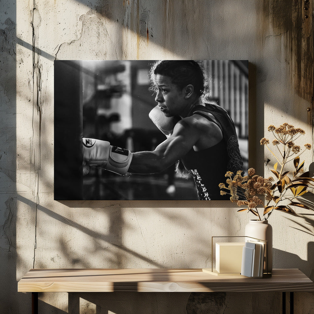 A dramatic black and white photo of a muscular female boxer in profile, intensely focused as she punches a heavy bag, set within a silver frame. Print