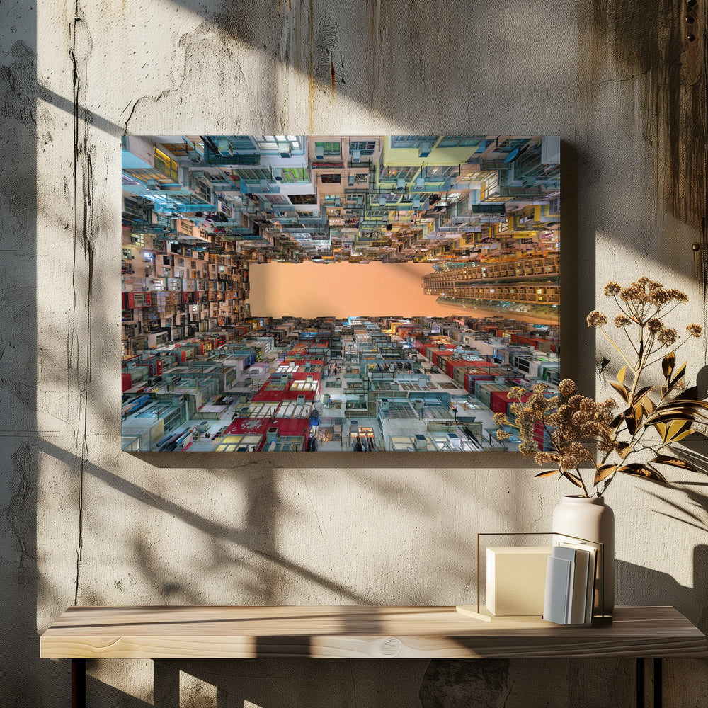 An upward-looking photograph from a courtyard surrounded by densely packed, multi-colored apartment buildings that create a rectangular frame around an orange sky. The unique perspective creates a surreal and geometric view of an urban landscape, all enclosed in a silver frame. Artwork