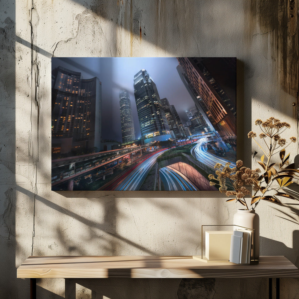 A dynamic, low-angle, long-exposure shot of a modern city at night. Towering skyscrapers with illuminated windows pierce through a foggy, dark blue sky. Below, curving highways are filled with the vibrant red and white light trails of moving traffic. Print