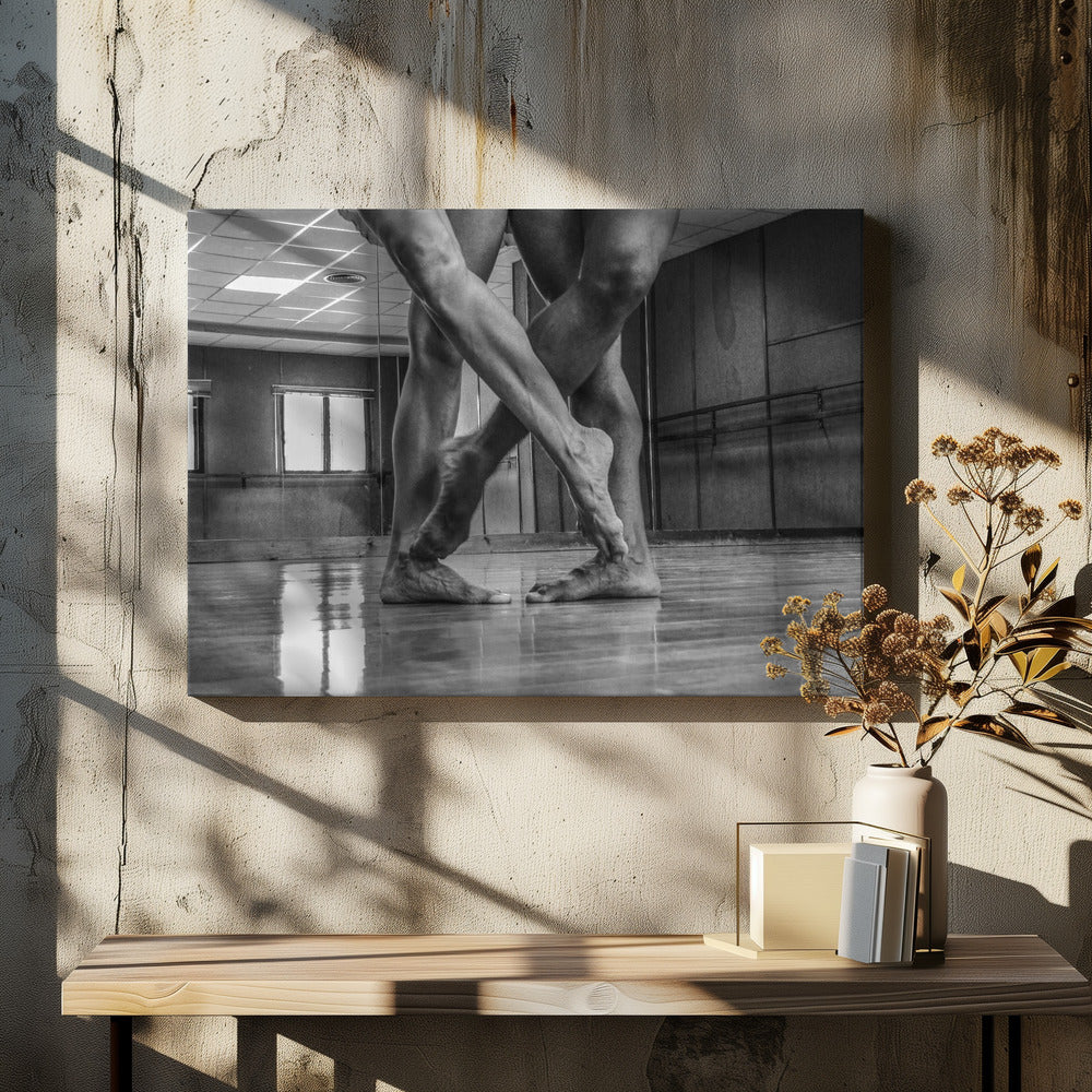 A dramatic low-angle, black and white photograph capturing the muscular legs and bare feet of two dancers intertwined in a dance studio. Their limbs cross in a display of strength and grace on a reflective wooden floor, with the studio's mirrored wall and barre visible in the background. The image is enclosed in a silver-grey frame. Decor